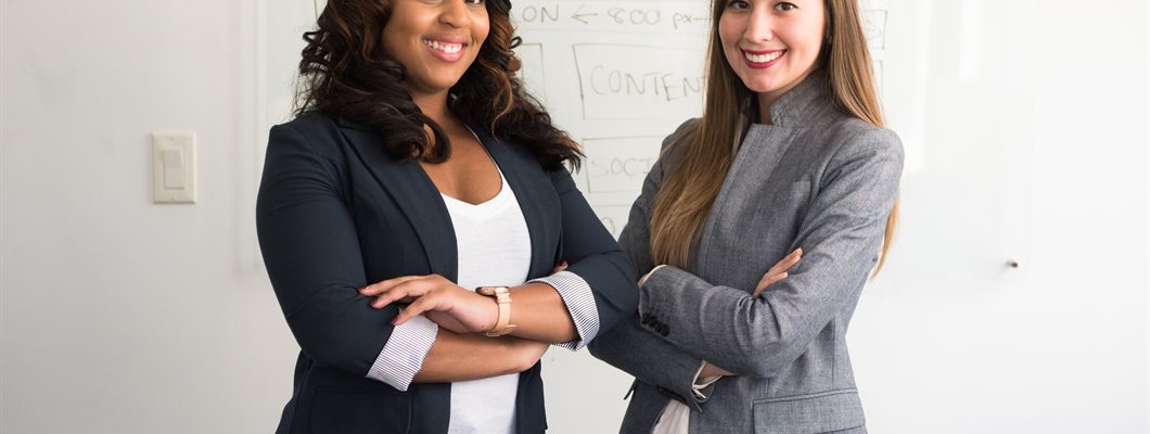 Two women stood in an office setting with crossed arms and smiles