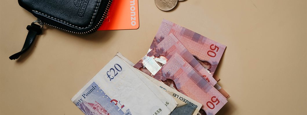 Bank notes on a table alongside coins, a bank card and a small wallet
