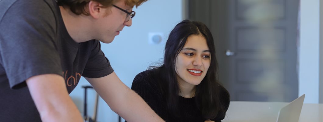 Two colleagues at work, looking at something on a laptop. Both people appear to be under 30 years old.